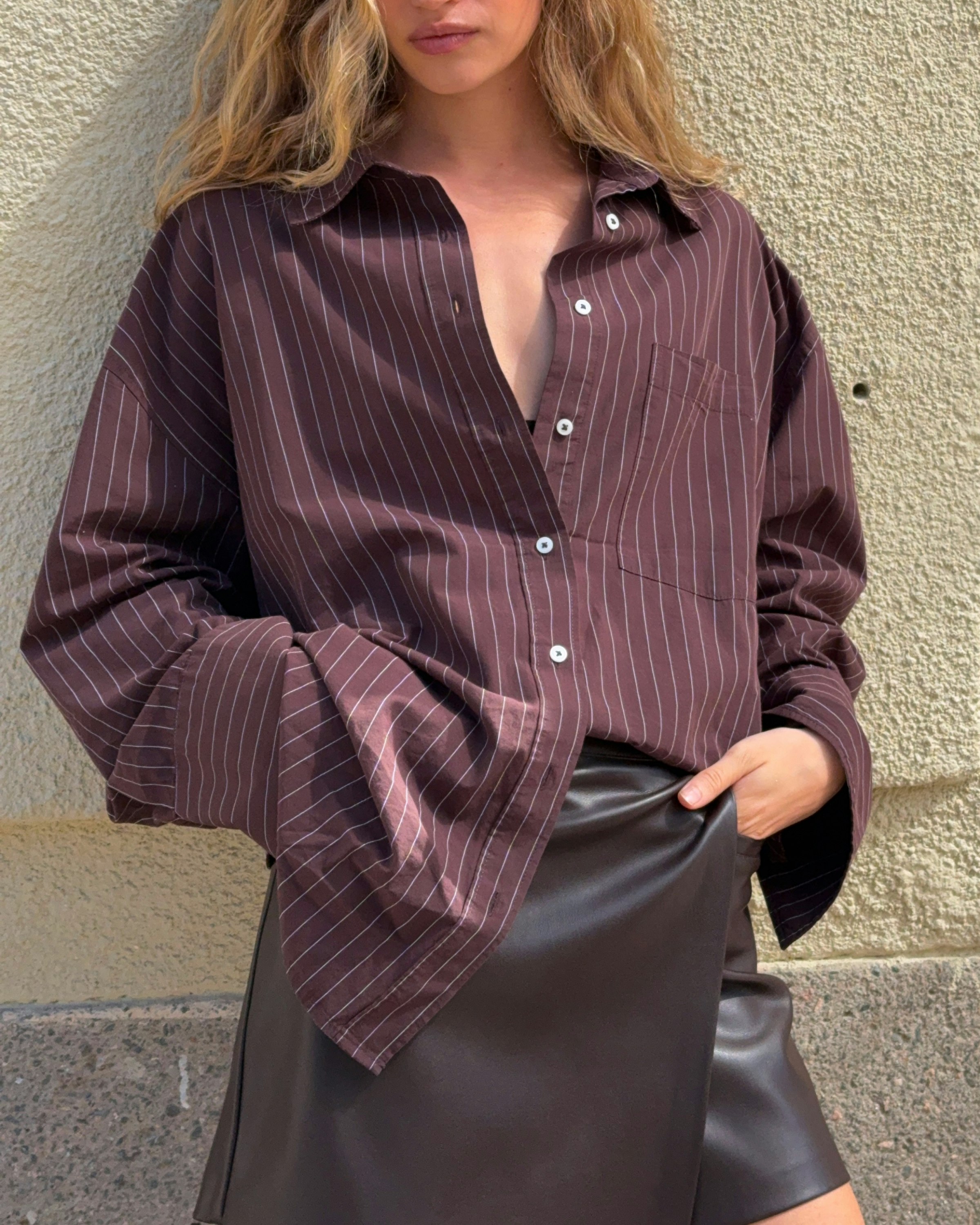 Brown pinstriped oversized shirt styled with a dark mini skirt.